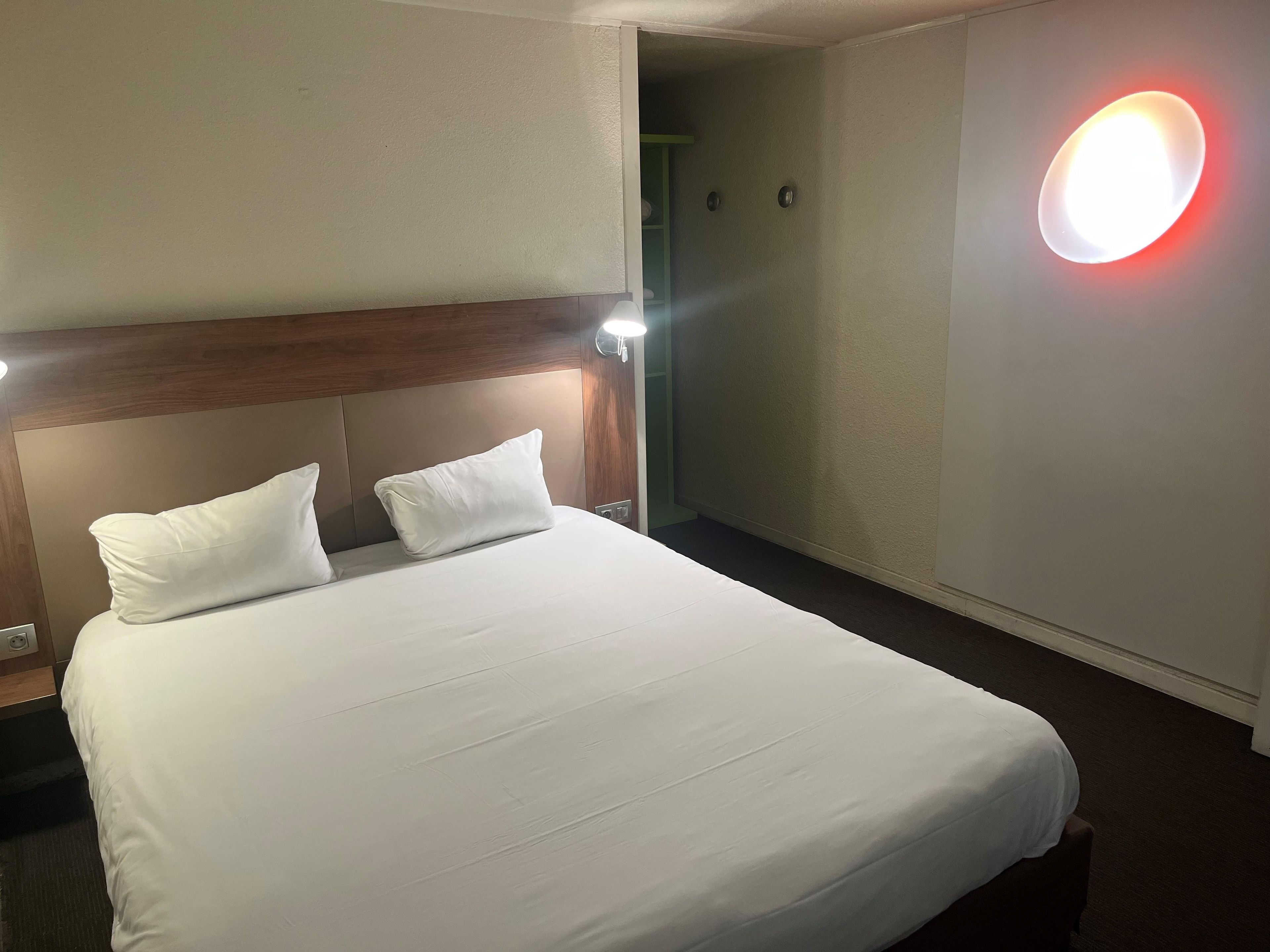 Habitación de hotel con una cama grande, dos almohadas, cabecera de madera y una lámpara fijada a la pared.