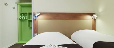 Une chambre d’hôtel avec un lit, une armoire verte et une lampe fixée au mur.