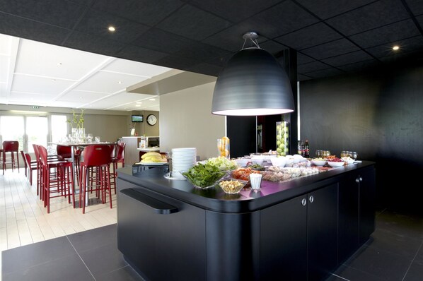 A modern kitchen with a central island, red chairs, and a large pendant light. - Campanile Lille Sud-CHR (Lille)