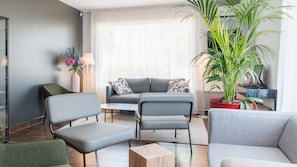Un salon moderne avec un canapé gris, deux fauteuils, une table basse et une grande plante en pot.
