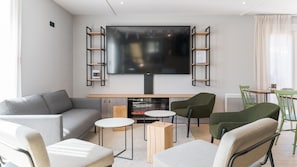 A modern living room with a flat-screen TV, a sofa, two chairs, a small table, and a fireplace. - Campanile NATURE - Lyon Est Aéroport Saint Exupéry (Saint-Laurent-de-Mure)