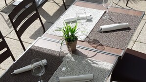 Un patio al aire libre con mesas y sillas, una planta en maceta y una mesa preparada con servilleta, vaso y cubiertos.