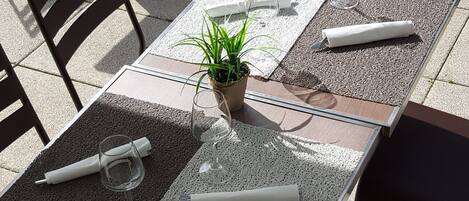 Un patio al aire libre con mesas y sillas, una planta en maceta y una mesa preparada con servilleta, vaso y cubiertos.