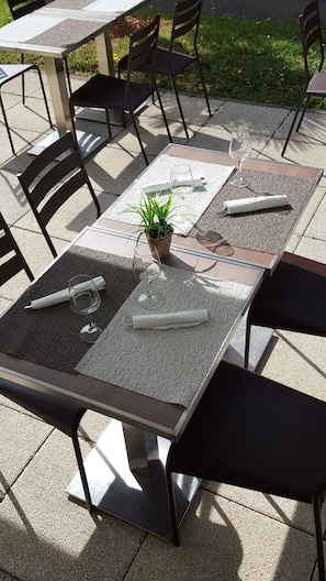 Un patio al aire libre con mesas y sillas, una planta en maceta y una mesa preparada con servilleta, vaso y cubiertos.