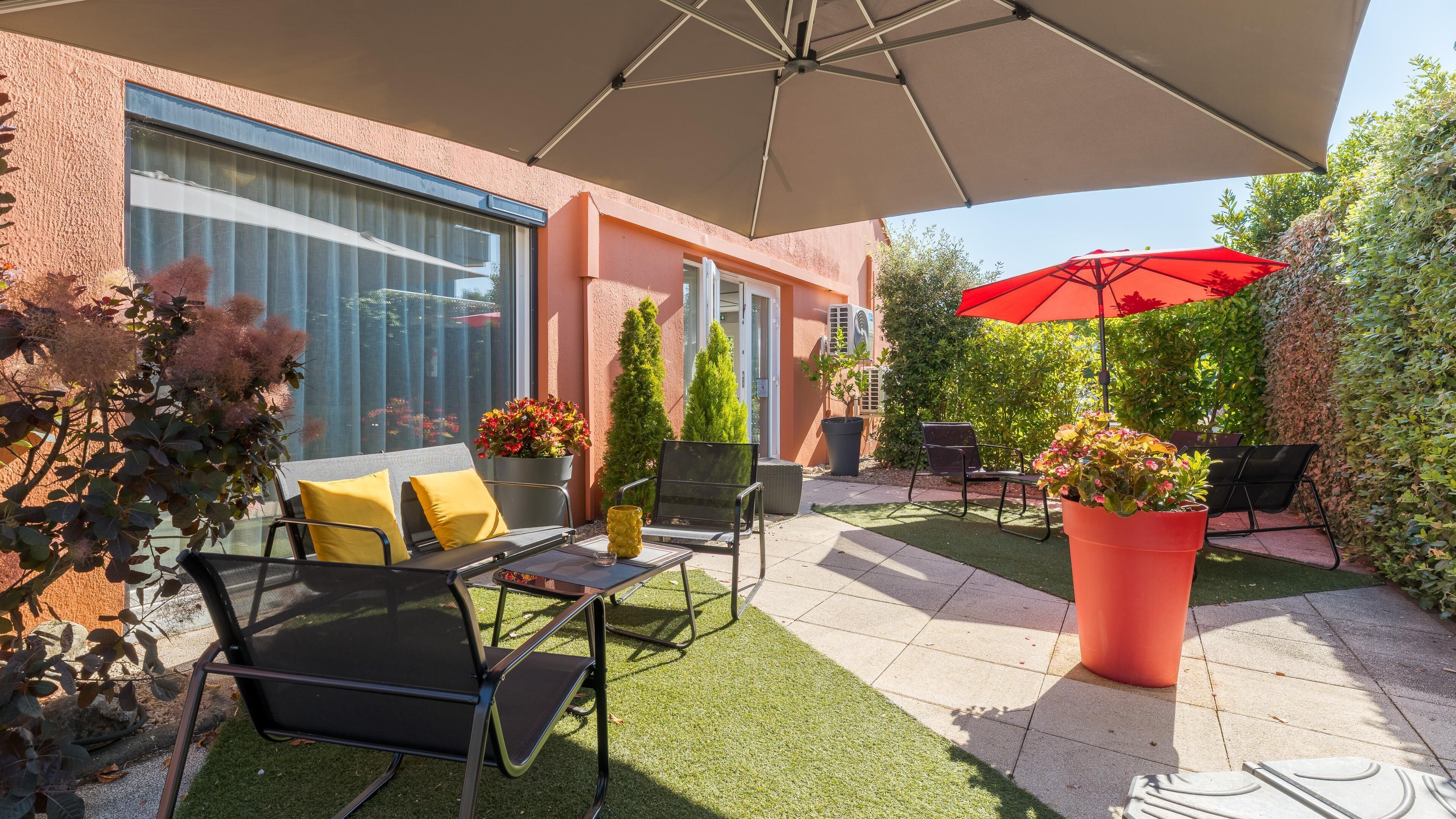 En udendørs terrasse med siddepladser, en stor parasol og plantekasser.