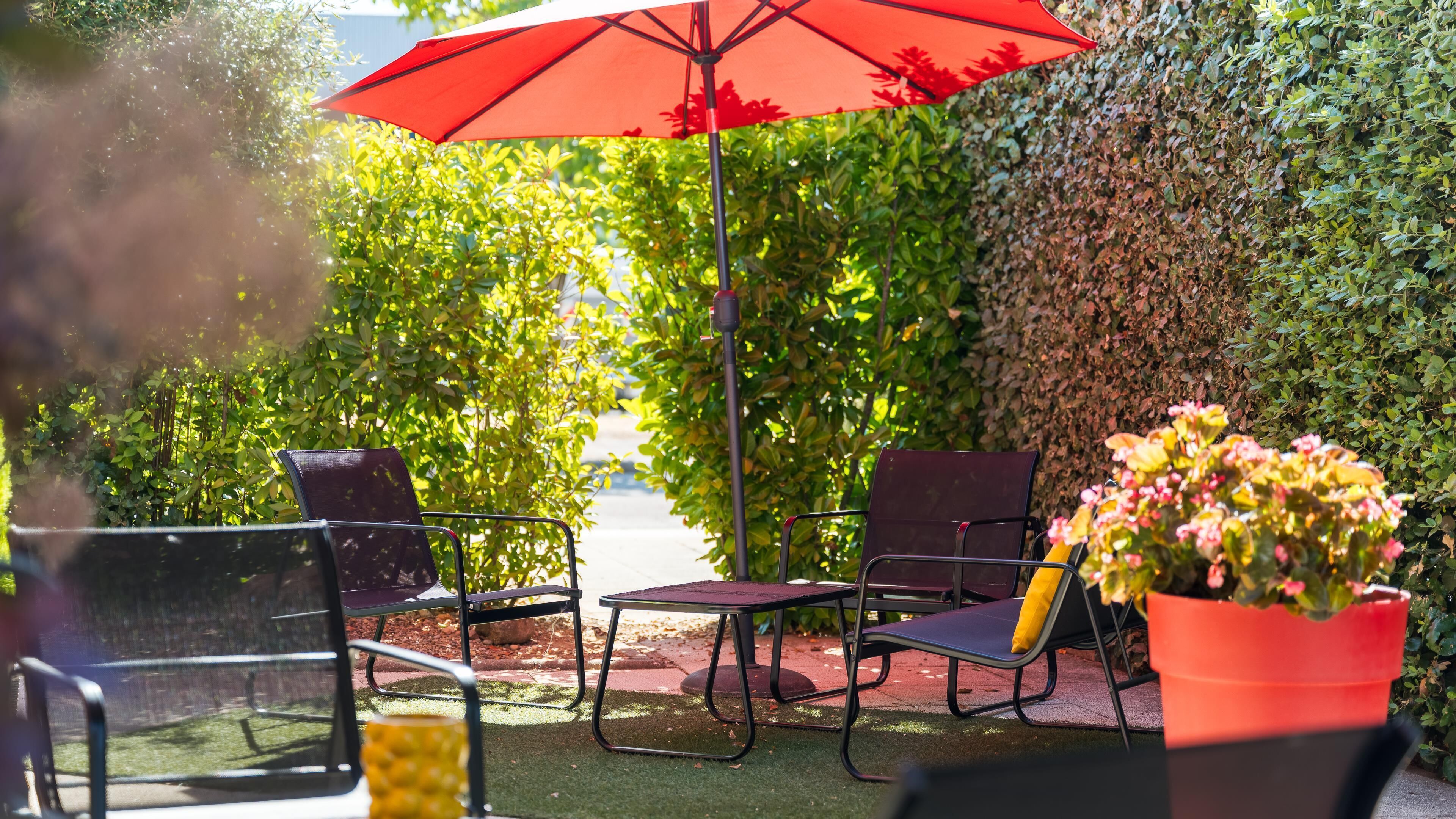 Un espace extérieur aménagé avec des chaises et une table, un parasol et une plante en pot.