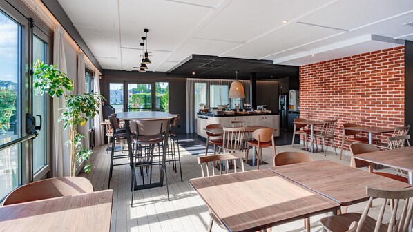 Un espace repas moderne avec un mur en briques, de grandes fenêtres et un îlot central doté de sièges.