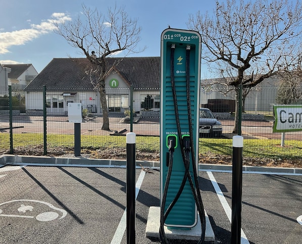 Un estacionamiento con estaciones de carga para vehículos eléctricos, un letrero de hotel y un área cercada con árboles.