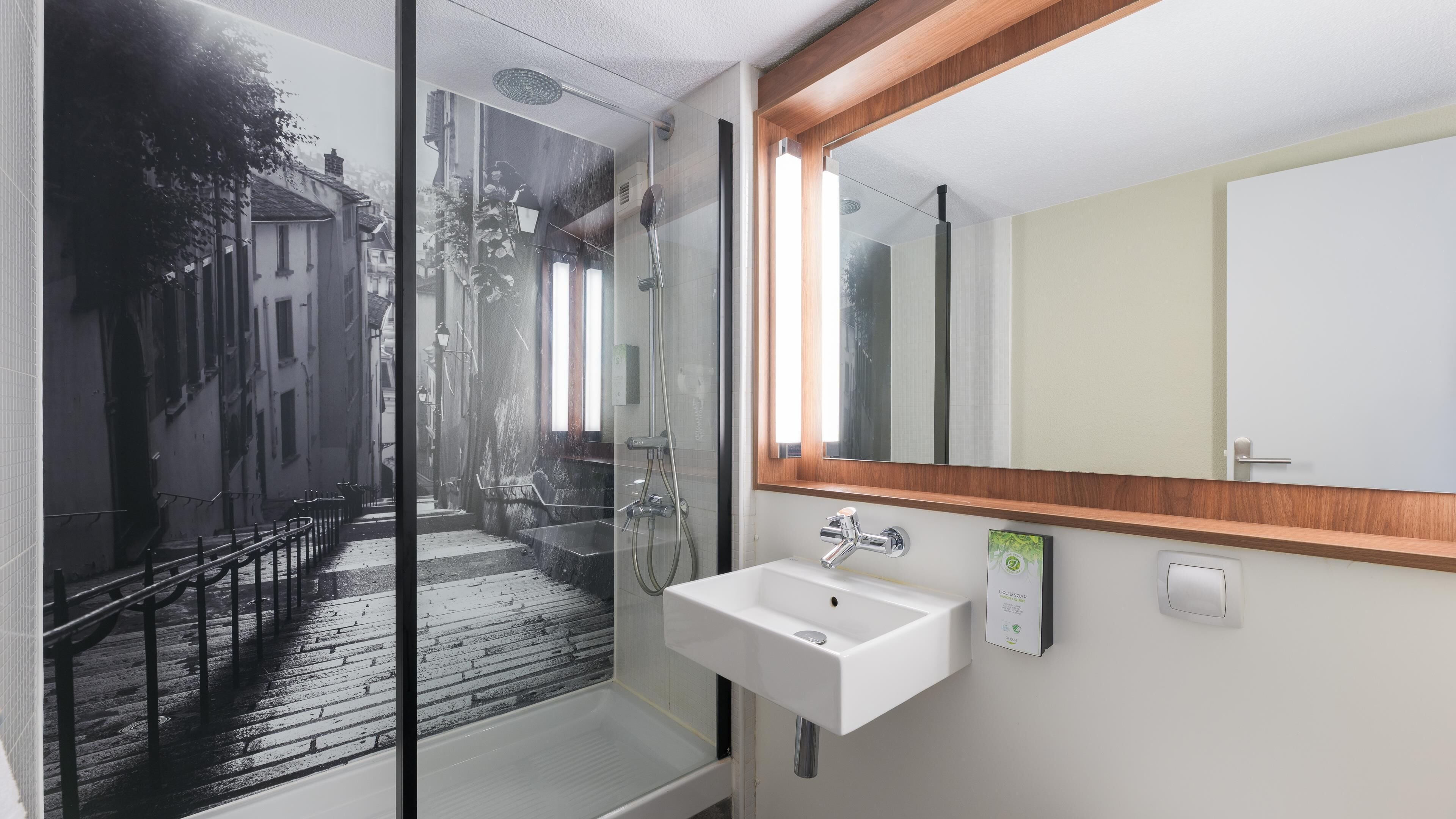 Un baño moderno con cabina de ducha de vidrio, un lavamanos blanco y un espejo con marco de madera.