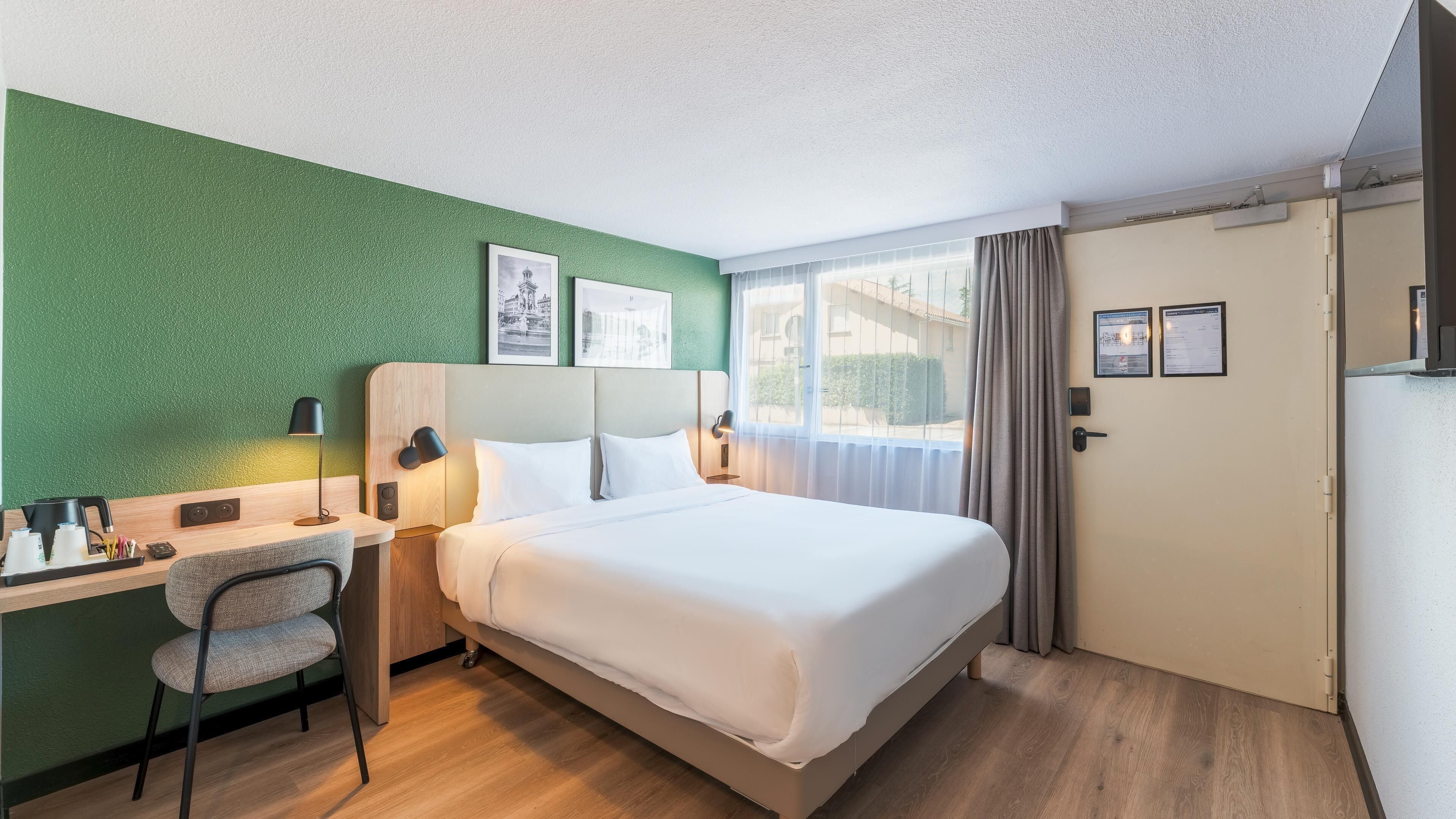 Ein Hotelzimmer mit Bett, Schreibtisch, Stuhl und Blick ins Freie.