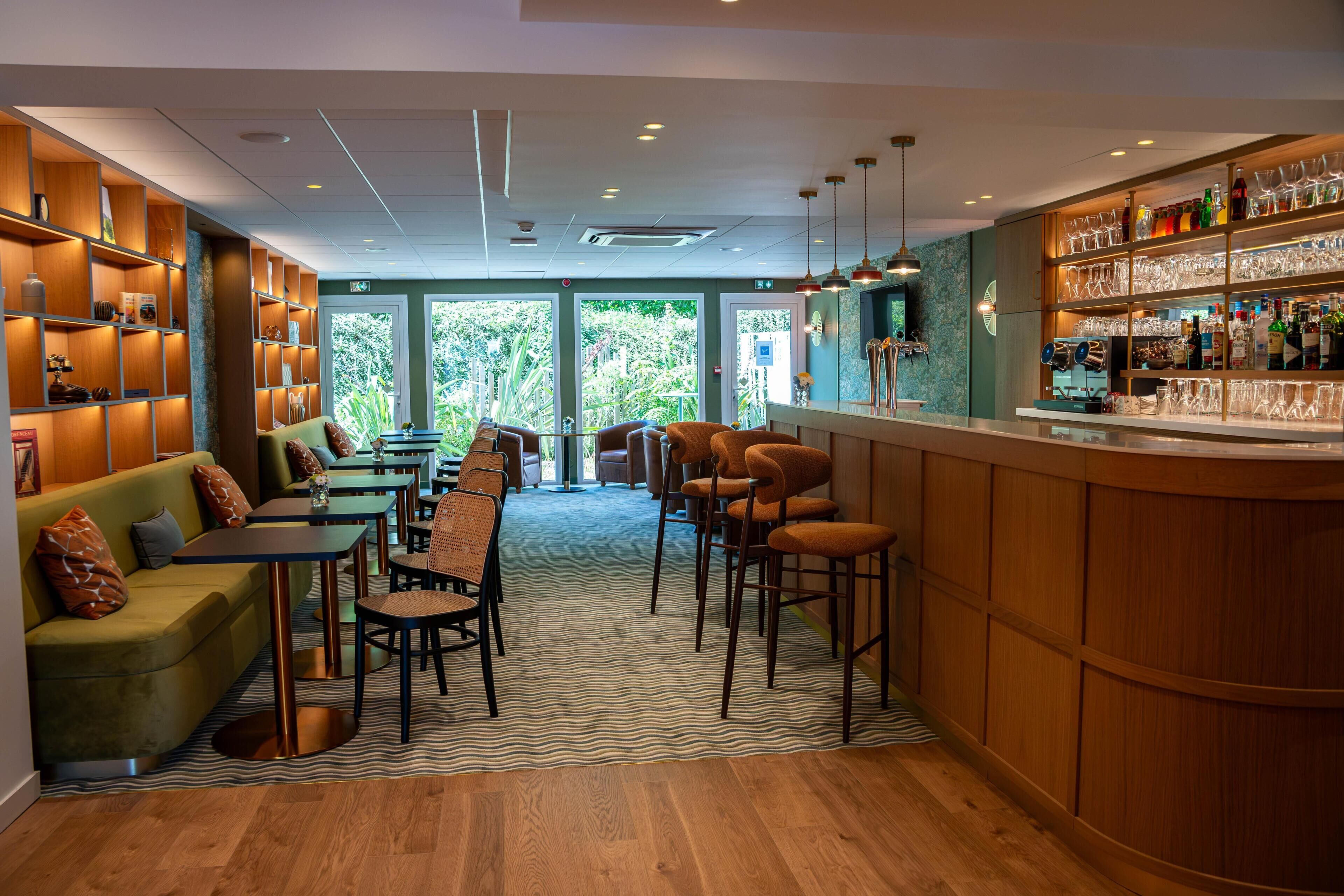 A bar area with wooden shelves, bar stools, and a counter. There are tables and chairs arranged for seating.