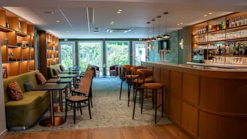 Un espace bar avec des étagères en bois, des tabourets et un comptoir. Des tables et des chaises sont disposées pour accueillir les clients.