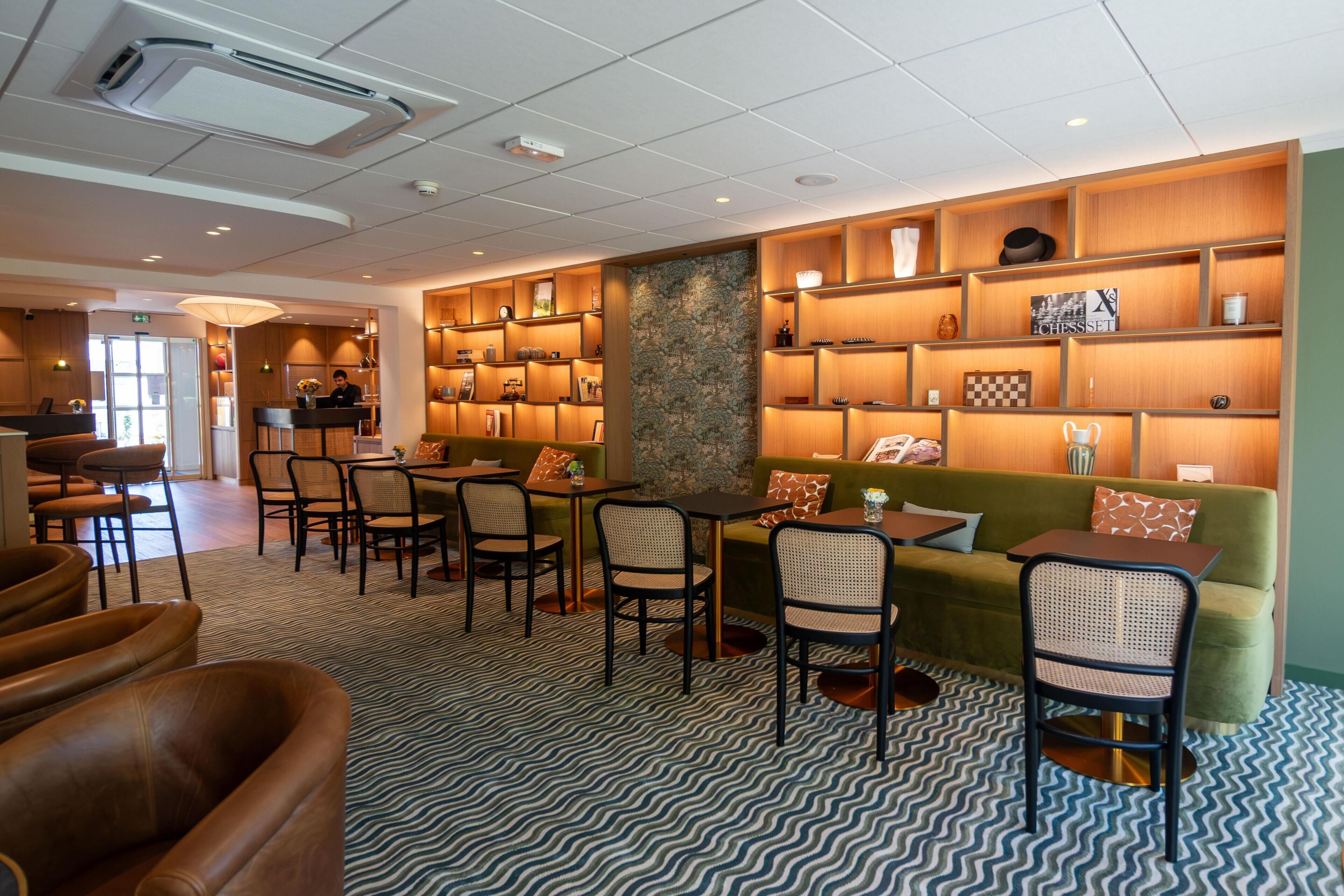 Et hotellobby med en receptionsdisk, et siddeområde med stole og borde, samt en væg med reoler der udstiller forskellige genstande.