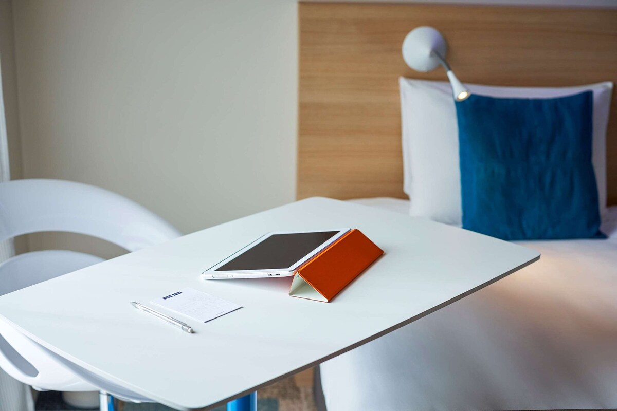 A neatly arranged hotel room with a white table, a tablet, a pen, and a notepad.