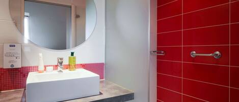 Un baño con lavamanos blanco, un espejo grande y paredes de azulejos rojos.