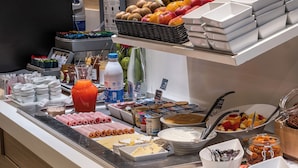 Buffet com diversos alimentos, incluindo frutas, queijos e acompanhamentos.