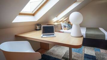 A modern room with a skylight, a desk with a laptop, a white chair, a bed with a green and white bedspread, and a decorative white object on the bed.