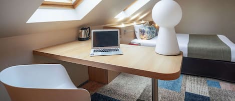 Una habitación moderna con tragaluz, un escritorio con una computadora portátil, una silla blanca, una cama con colcha verde y blanca, y un objeto decorativo blanco sobre la cama.