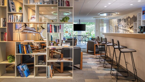Uma biblioteca moderna com estantes, áreas de estar e um bar com bancos.