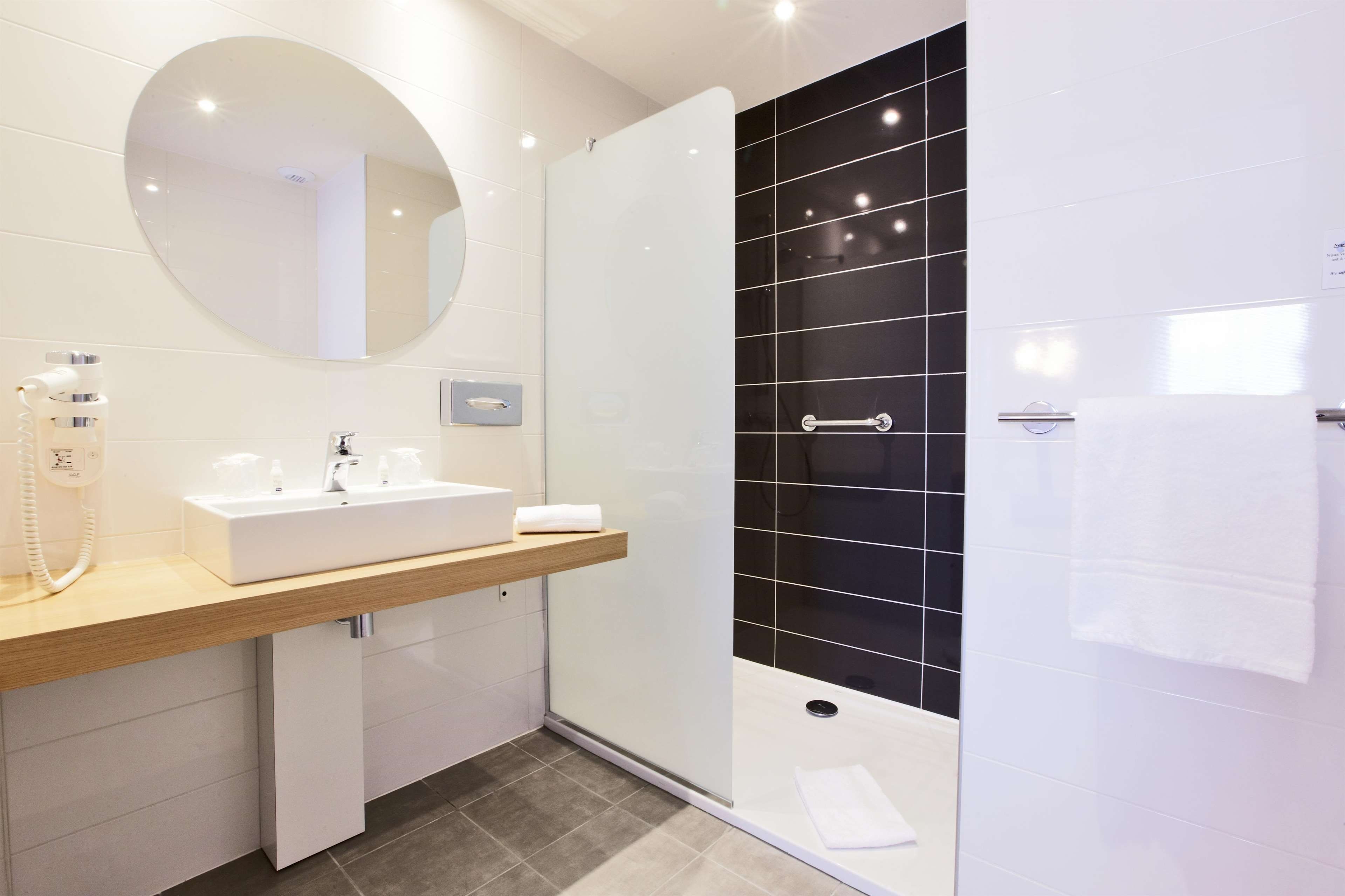 A modern bathroom with a white sink, a mirror, a handheld showerhead, and a black tiled shower enclosure.