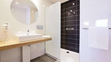 A modern bathroom with a white sink, a mirror, a handheld showerhead, and a black tiled shower enclosure.
