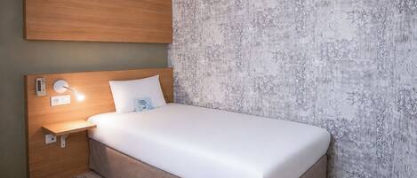 Habitación de hotel con cama, mesita de noche, aire acondicionado en la pared y alfombra estampada.