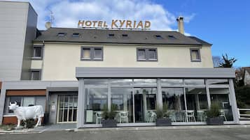 A hotel named "HOTEL KYRIAD" with a modern facade, large windows, and outdoor seating area.