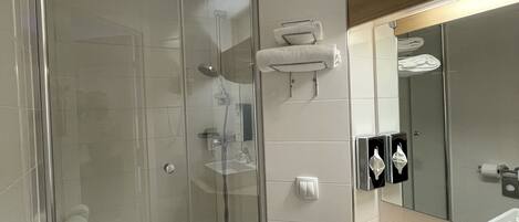 Un baño moderno con ducha de vidrio, inodoro y lavamanos con espejo.