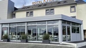 Um hotel moderno com fachada de vidro, área de estar ao ar livre e uma placa com a inscrição 'HOTEL KYRIAD'.