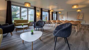Een moderne vergaderruimte met een combinatie van banken en stoelen, een witte tafel en grote ramen met uitzicht op het omliggende landschap.