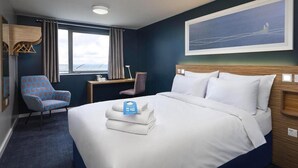 Habitación de hotel con cama, escritorio, silla, ventana con cortinas y un cuadro en la pared.