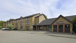 Un edificio de ladrillo con un letrero de Traveltodge, un estacionamiento y un cielo despejado.