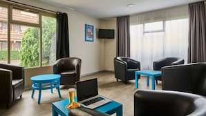 A modern hotel room with leather chairs, a blue table, a laptop, and a TV on the wall.