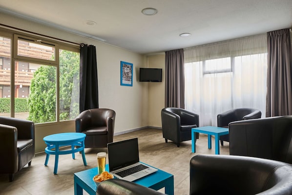 A modern hotel room with leather chairs, a blue table, a laptop, and a TV on the wall.