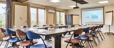 Un salón de conferencias con una larga mesa, sillas, una pantalla de proyector y una pizarra.