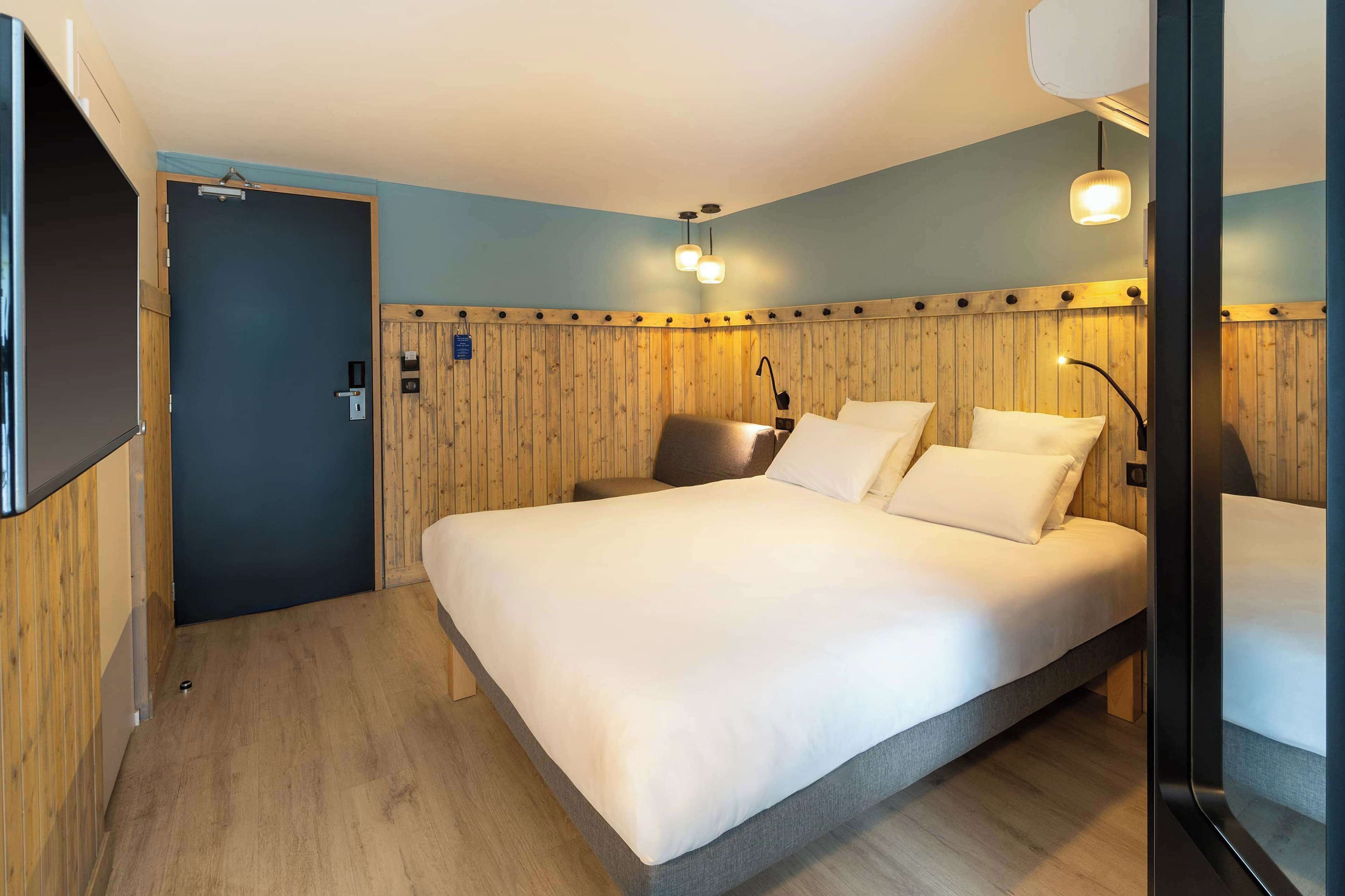 Een slaapkamer met een groot bed, houten paneelwanden en een wandgemonteerde flatscreen televisie.