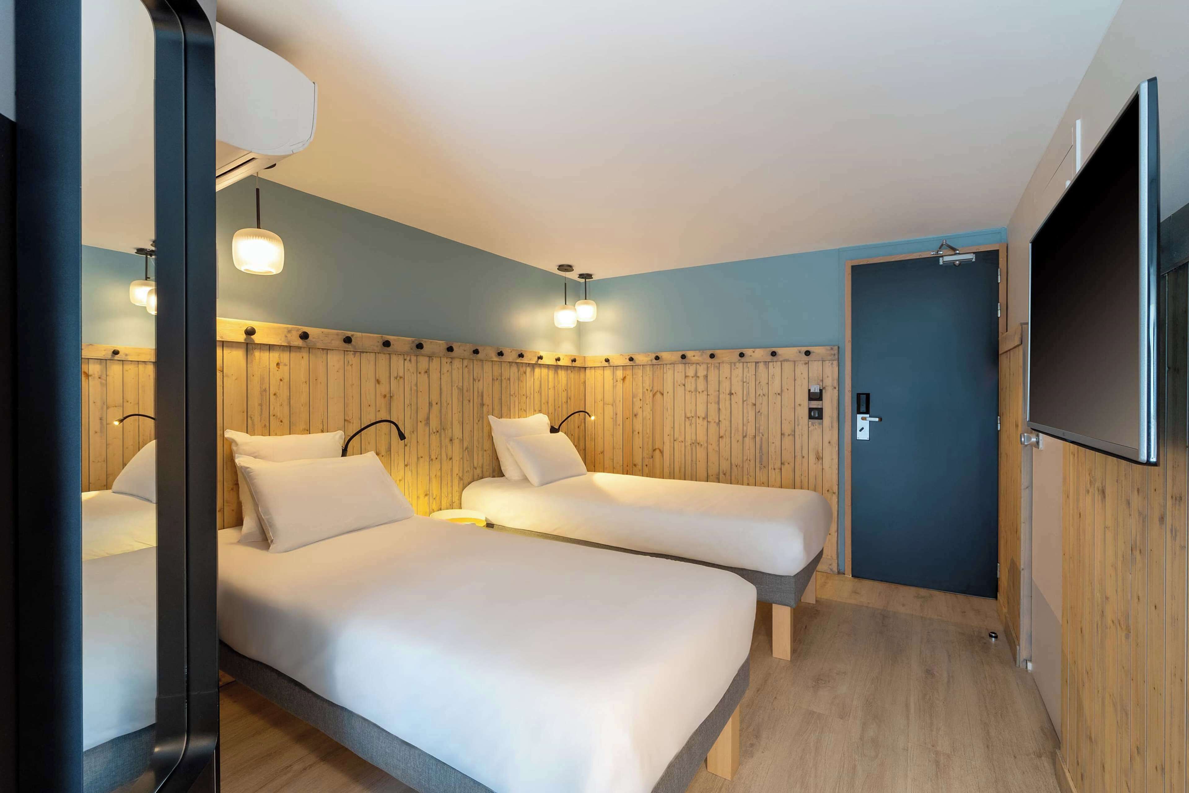 A hotel room with two beds, wooden paneling on the walls, and a flat-screen TV mounted on the wall.
