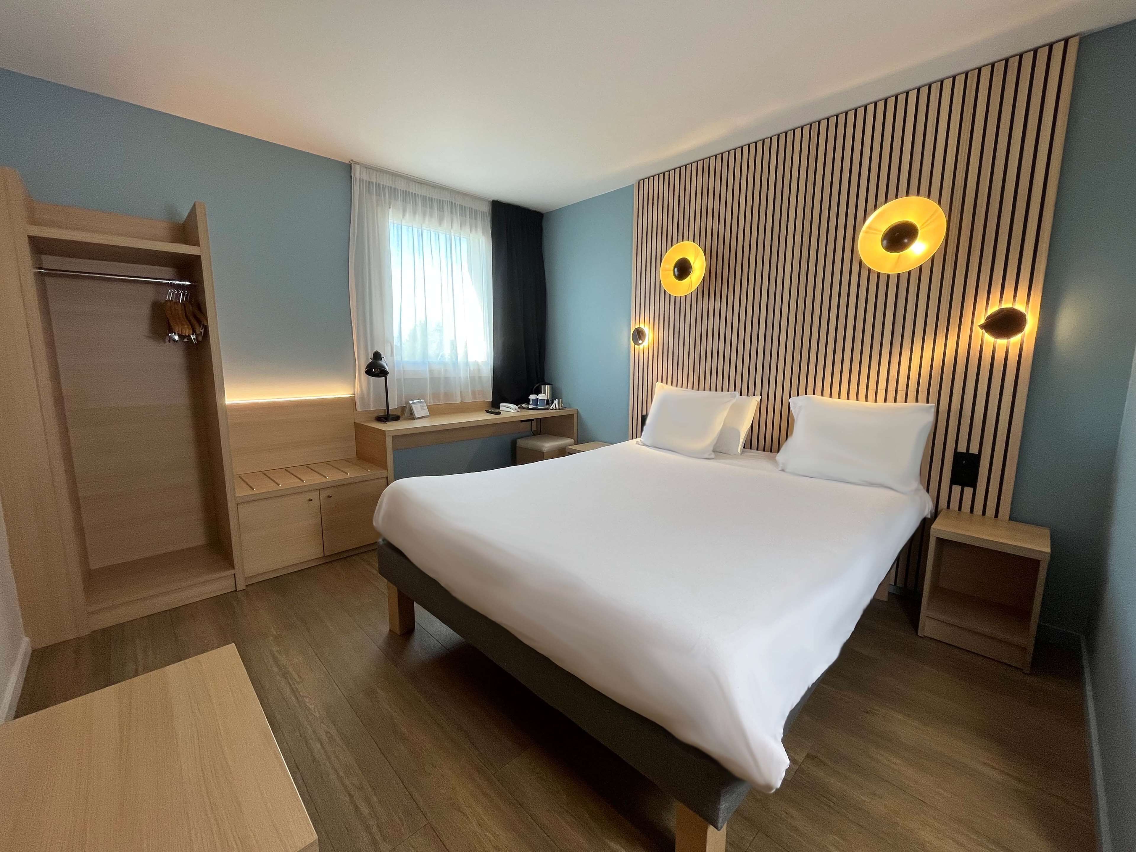 A modern hotel room with a large bed, a desk, a vanity, and a shower.