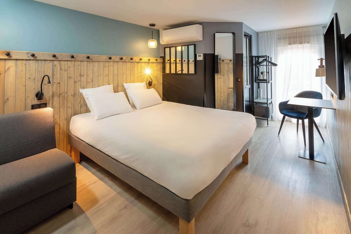 A modern hotel room with a large bed, a sofa, a desk, and a TV.