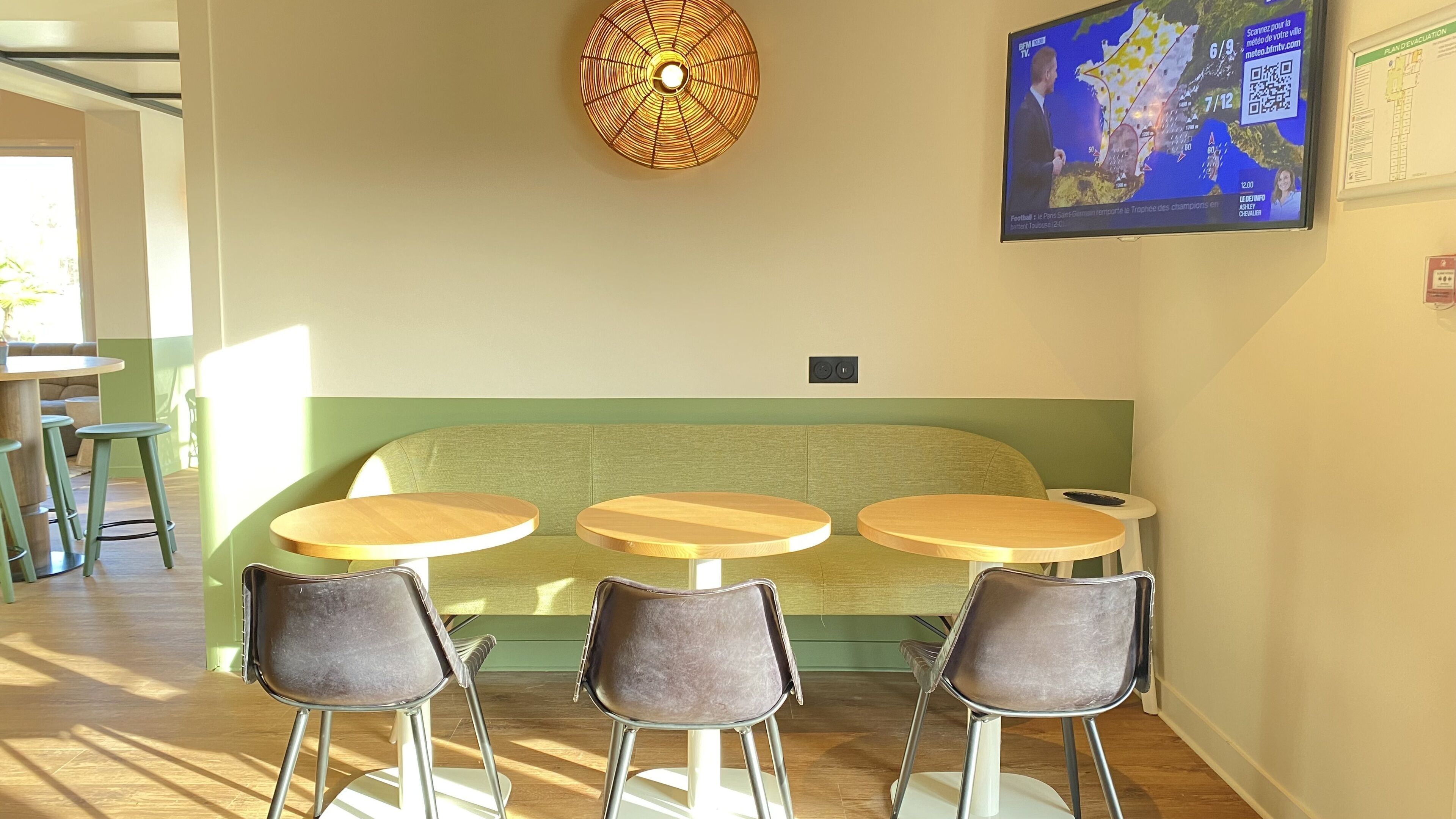 A seating area with a green cushioned bench and three round tables, each with a chair.