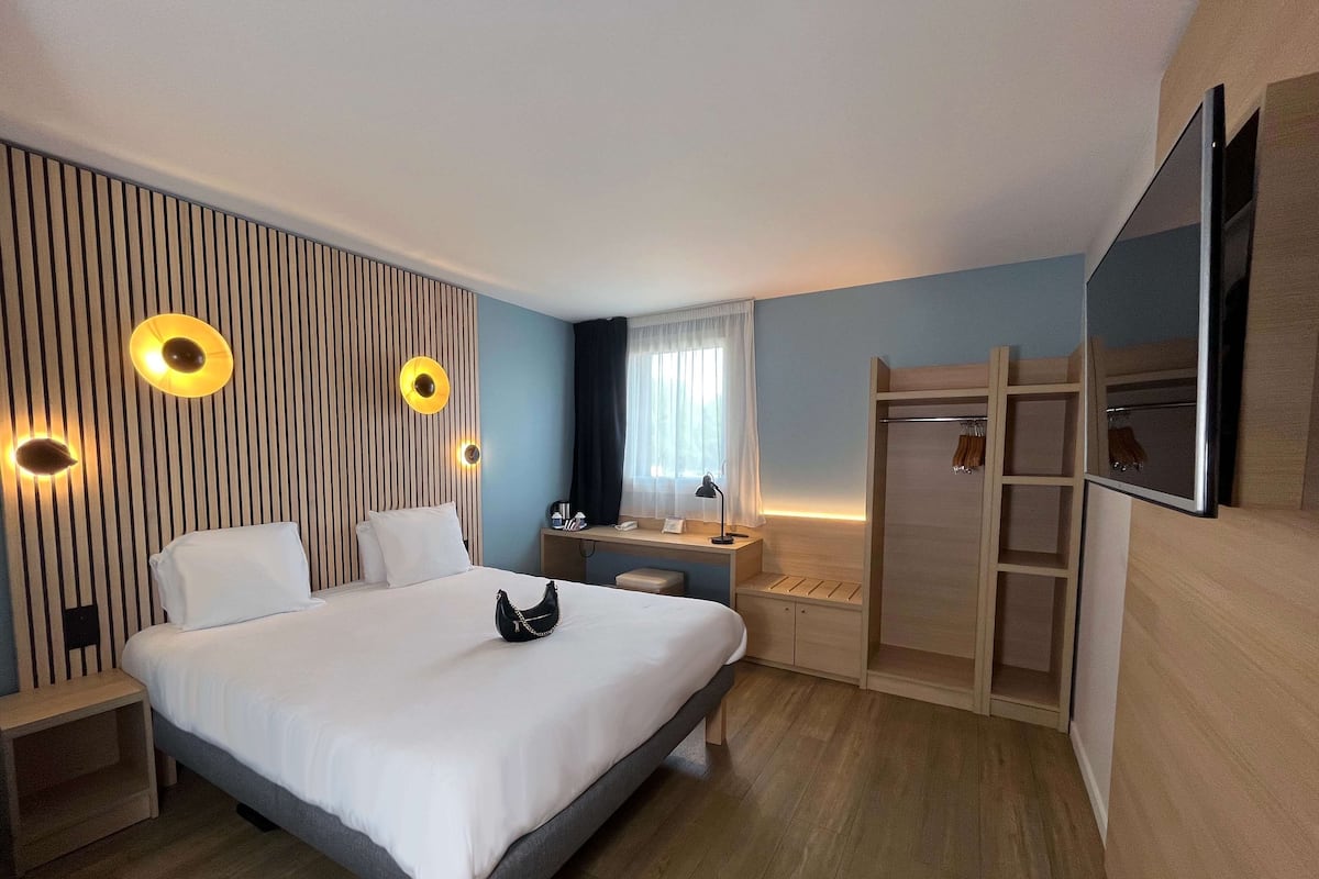 A modern hotel room with a bed, desk, and wardrobe.