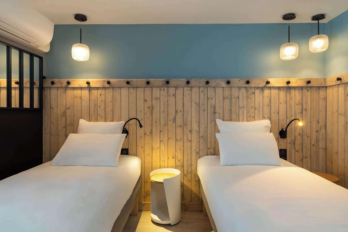 A room with two beds, wooden paneling on the walls, and pendant lights.