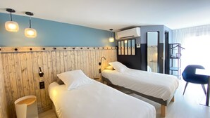 Hotellihuone, jossa on kaksi sänkyä, puinen pääty, pieni pöytä, tuoli, ilmastointilaite ja peili.