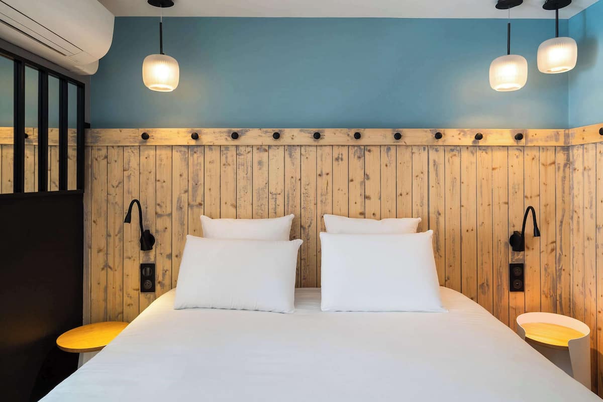 A hotel room with a wooden panel wall, a large bed with white bedding, two bedside tables with lamps, and a ceiling light fixture.