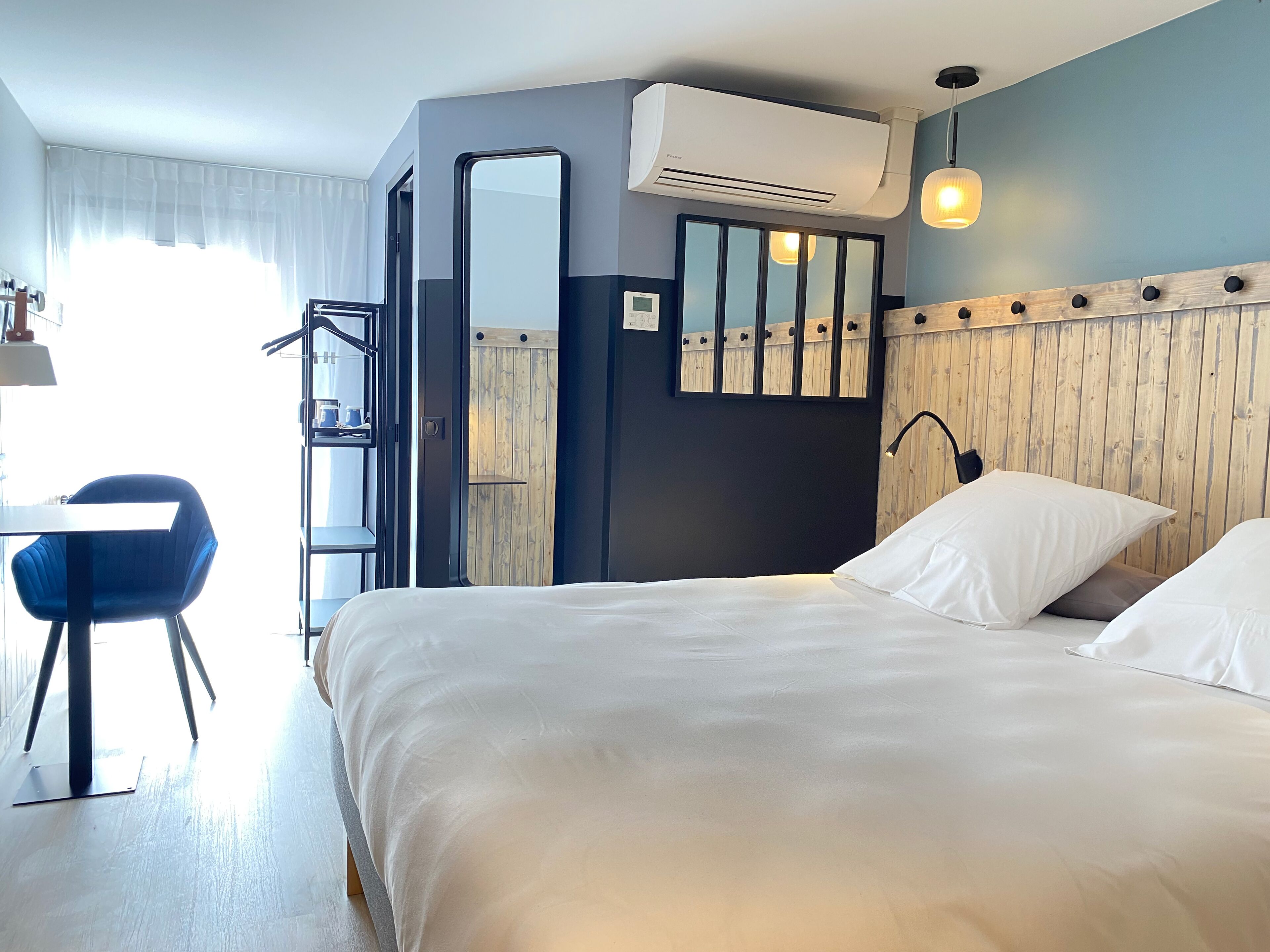A hotel room with a bed, a desk, a chair, and a large mirror.
