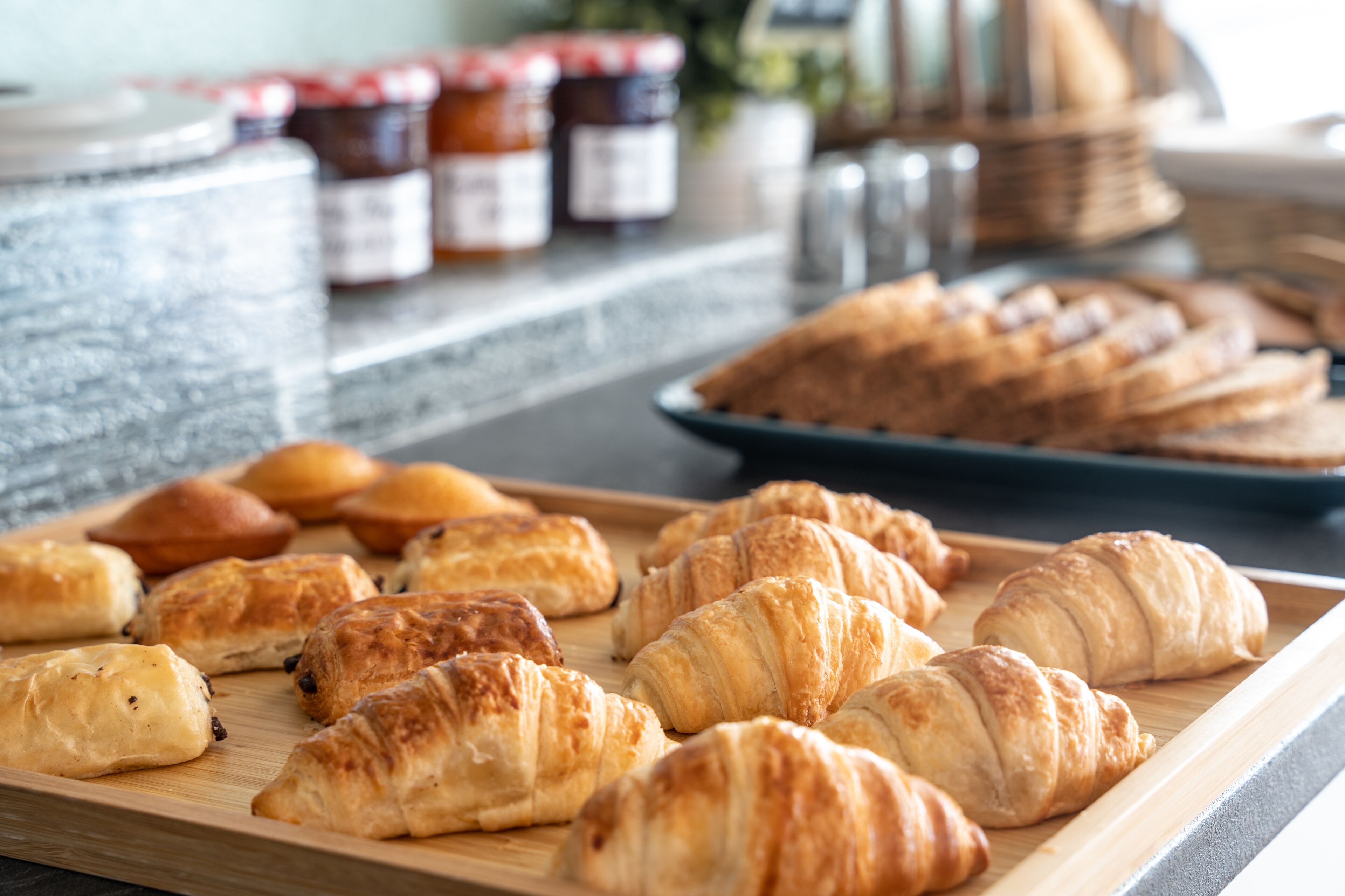 A wooden board with assorted pastries, including croissants and muffins, on a kitchen counter.
