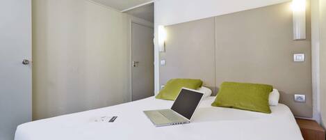 A hotel room with a bed, a laptop, and a green pillow.