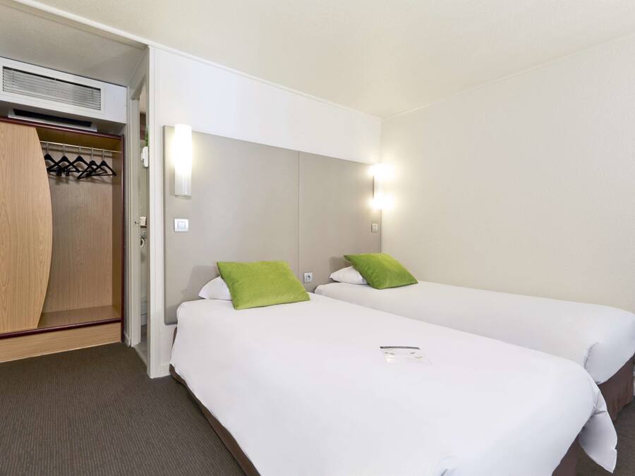 Een hotelkamer met twee bedden, een houten kledingkast en een wandradiator.