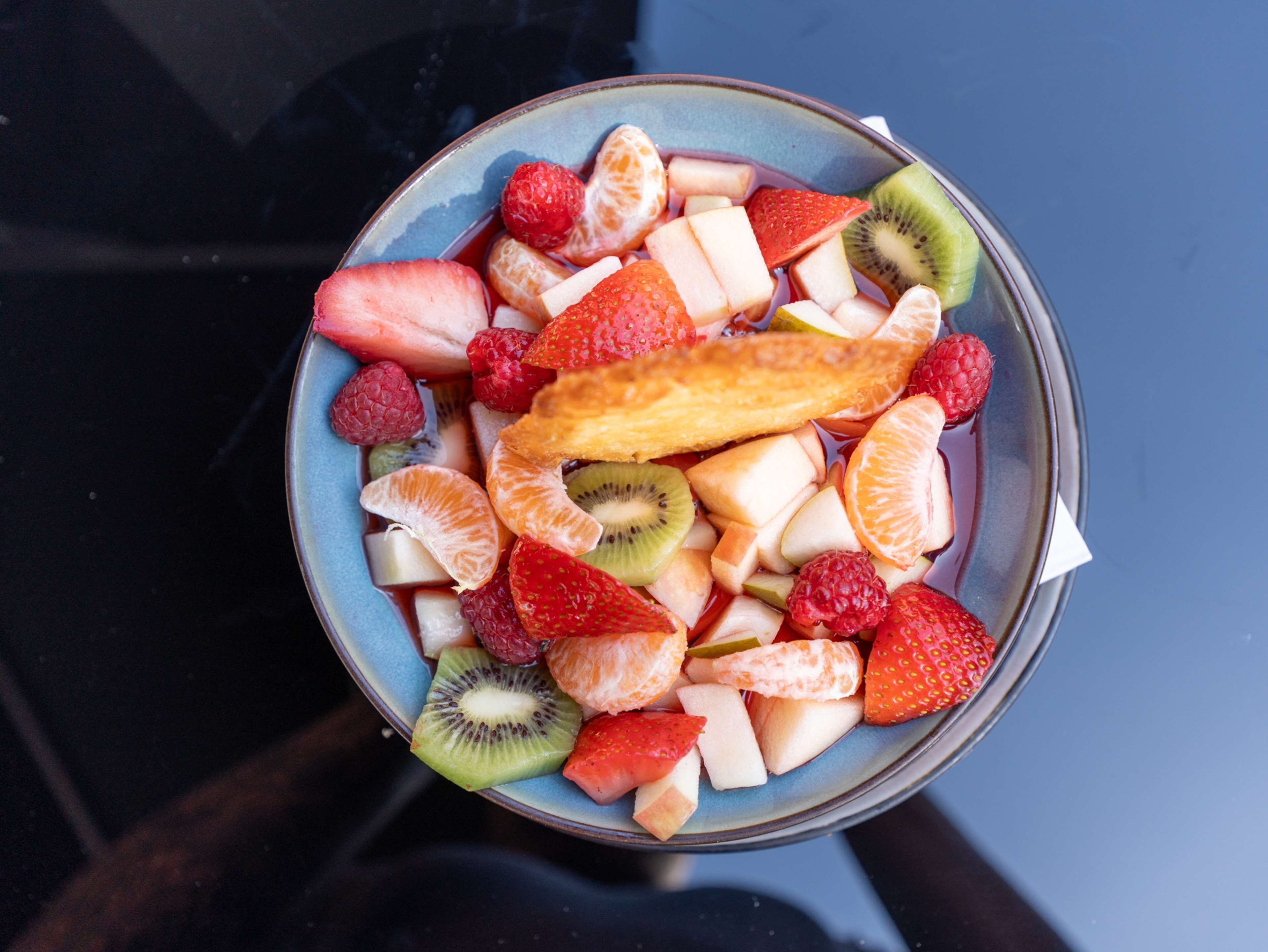 A bowl of assorted fruits including strawberries, kiwi, oranges, and raspberries.