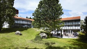 A building with a red-tiled roof, a covered outdoor seating area, and a grassy courtyard with rocks and trees. - Kyriad Lyon Sud Sainte Foy (Sainte-Foy-les-Lyon)